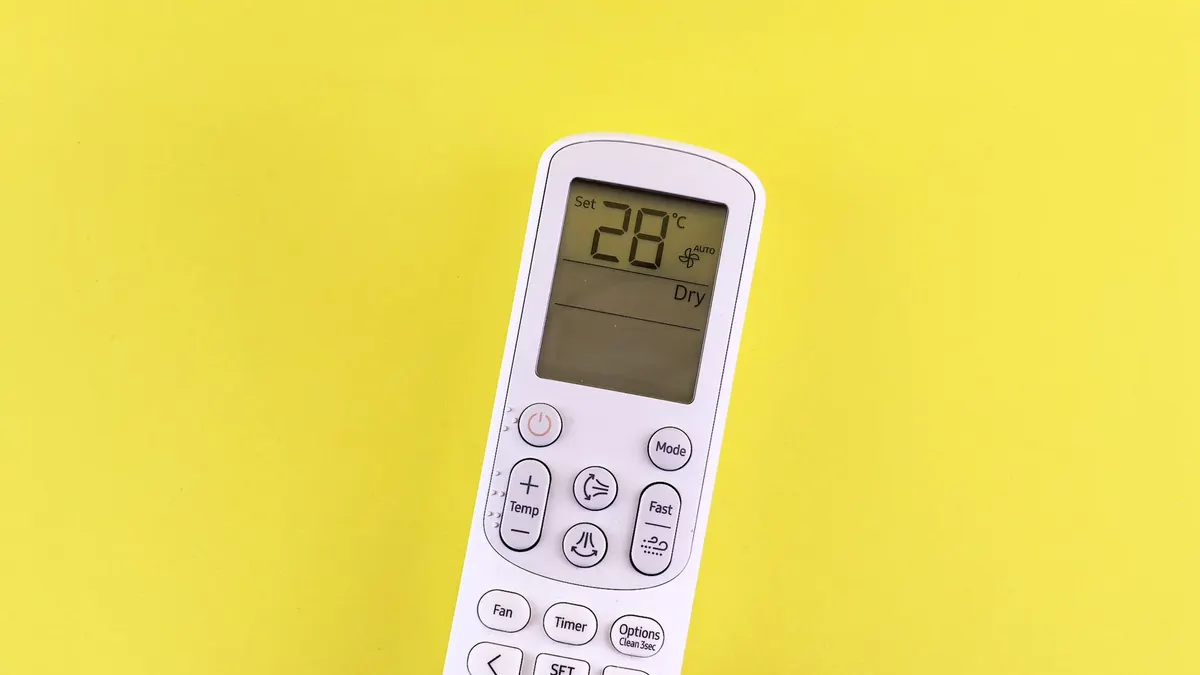 Air conditioner remote with temperature set at 28°C on a yellow background.