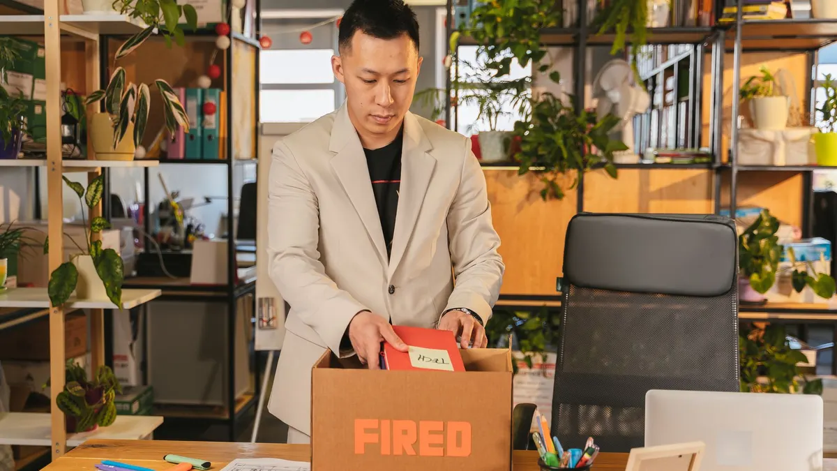 An adult man pack personal items after receiving a fired notice in an office setting, expressing corporate life challenges.