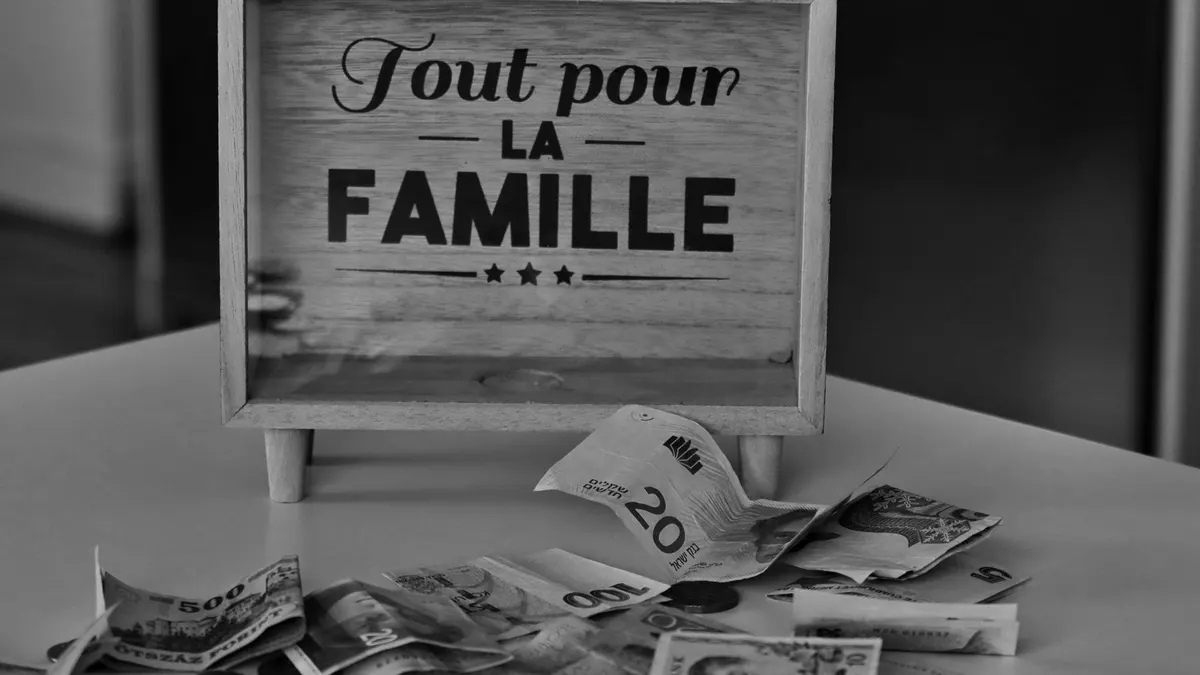 Black and white photo of a money box and various currencies on a table, symbolizing savings for family.