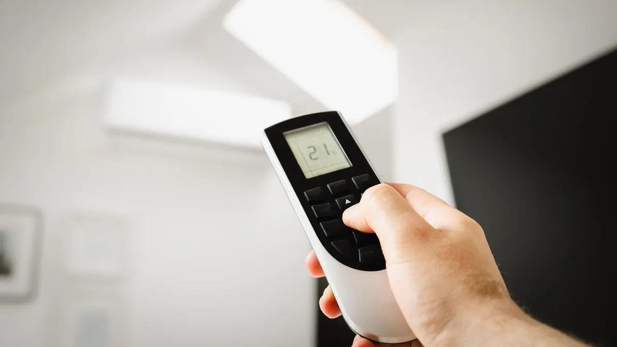 Close-up of a man using a remote to control air conditioning indoors.