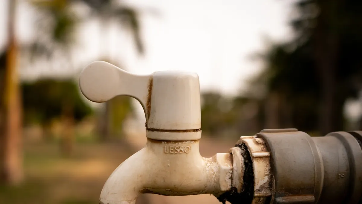 A close-up shot of a water droplet falling from an outdoor tap, highlighting water conservation issues.