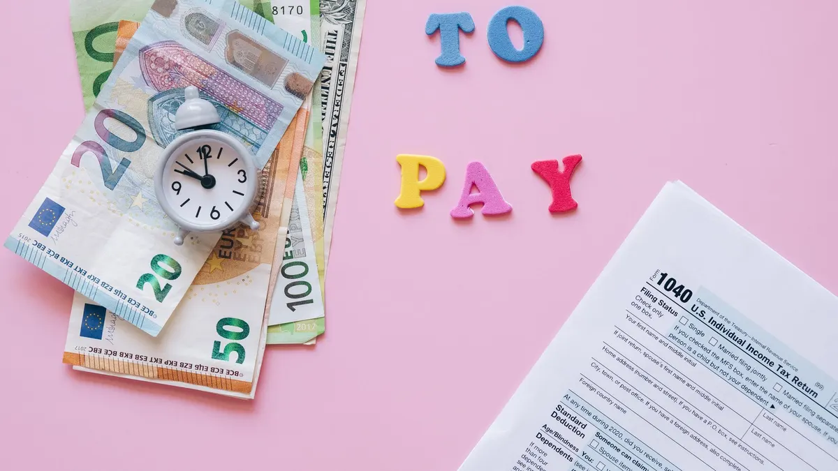 Flat lay of taxes, currency, and reminder to pay on pink background.
