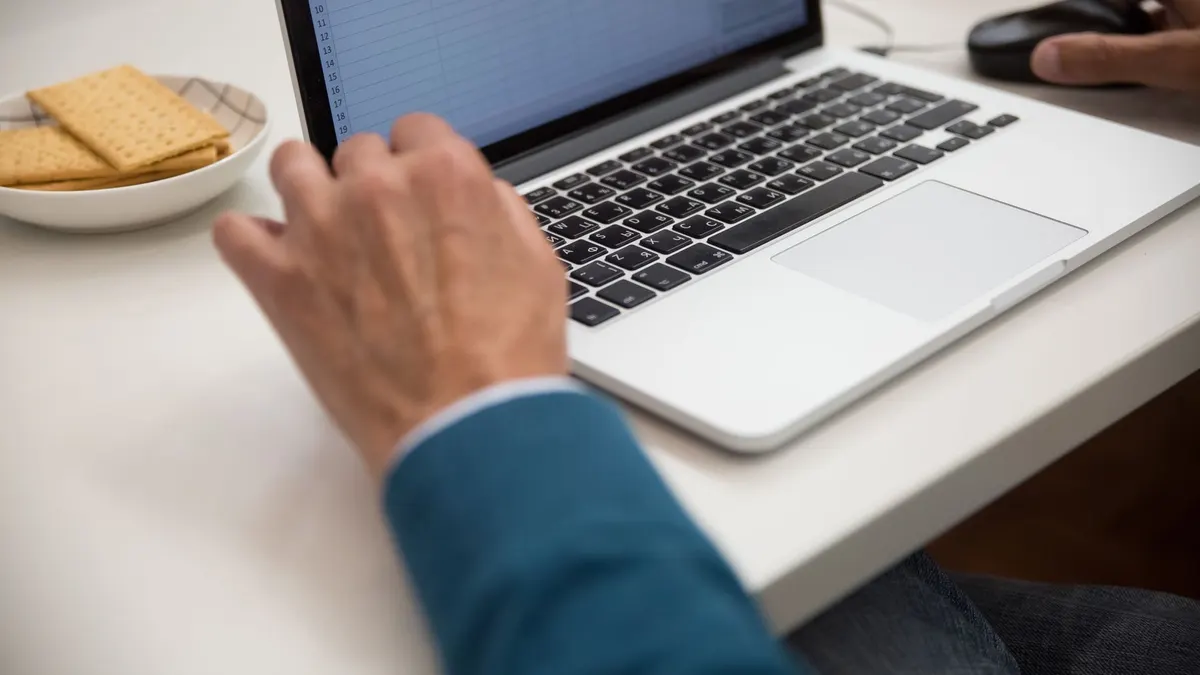A person working on a laptop at a desk with snacks, emphasizing productivity and technology.