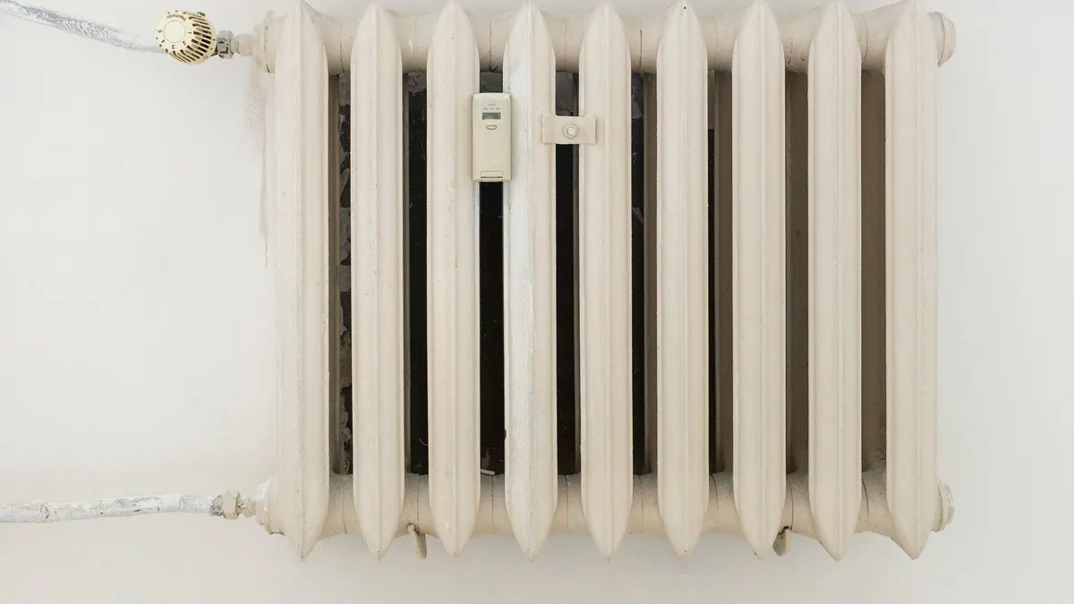 A classic white metal radiator on a plain wall, showcasing minimalist interior design.