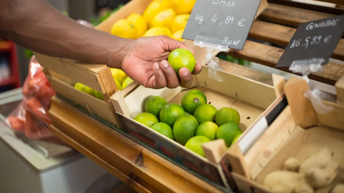 A close-up of a hand picking limes at a market in Portugal, displaying price in euros.