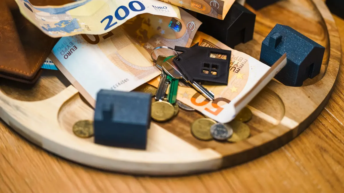 Euro currency, keys, and miniature houses symbolize real estate and finance concepts.