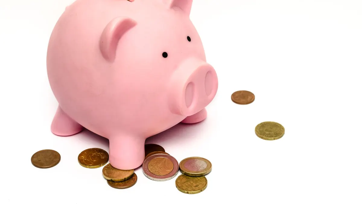 A pink piggy bank surrounded by scattered coins, symbolizing savings and financial investment.
