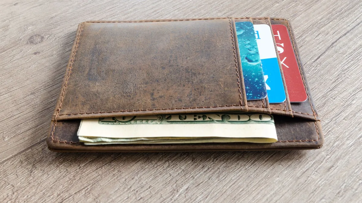 A brown leather wallet with cash and credit cards on a wooden surface.