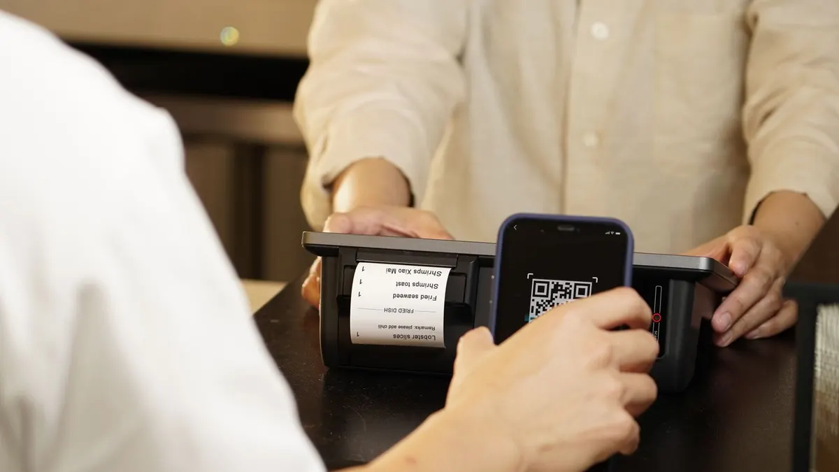 Two individuals engaged in a contactless payment using a QR code scanner at a retail counter.
