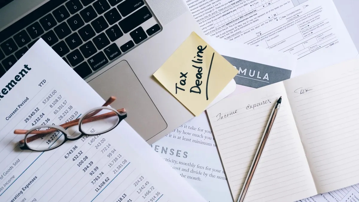 Workspace with laptop, documents, and tax deadline note for financial management.