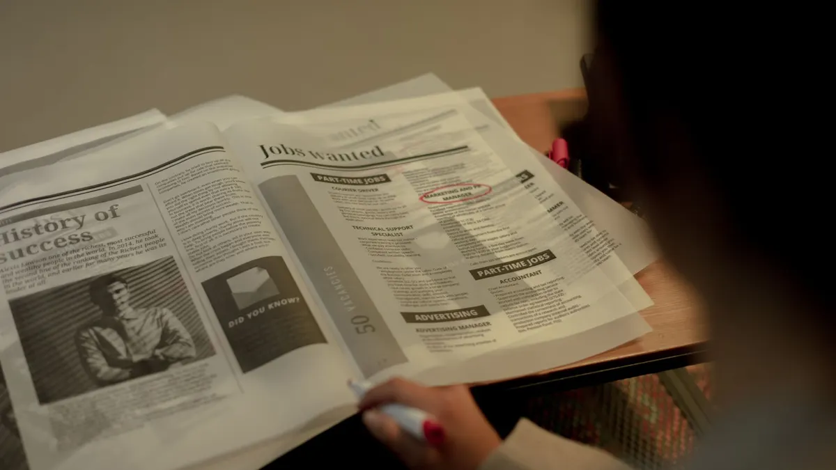 Person reviewing job listings in a newspaper, holding a pink marker for highlighting job ads.