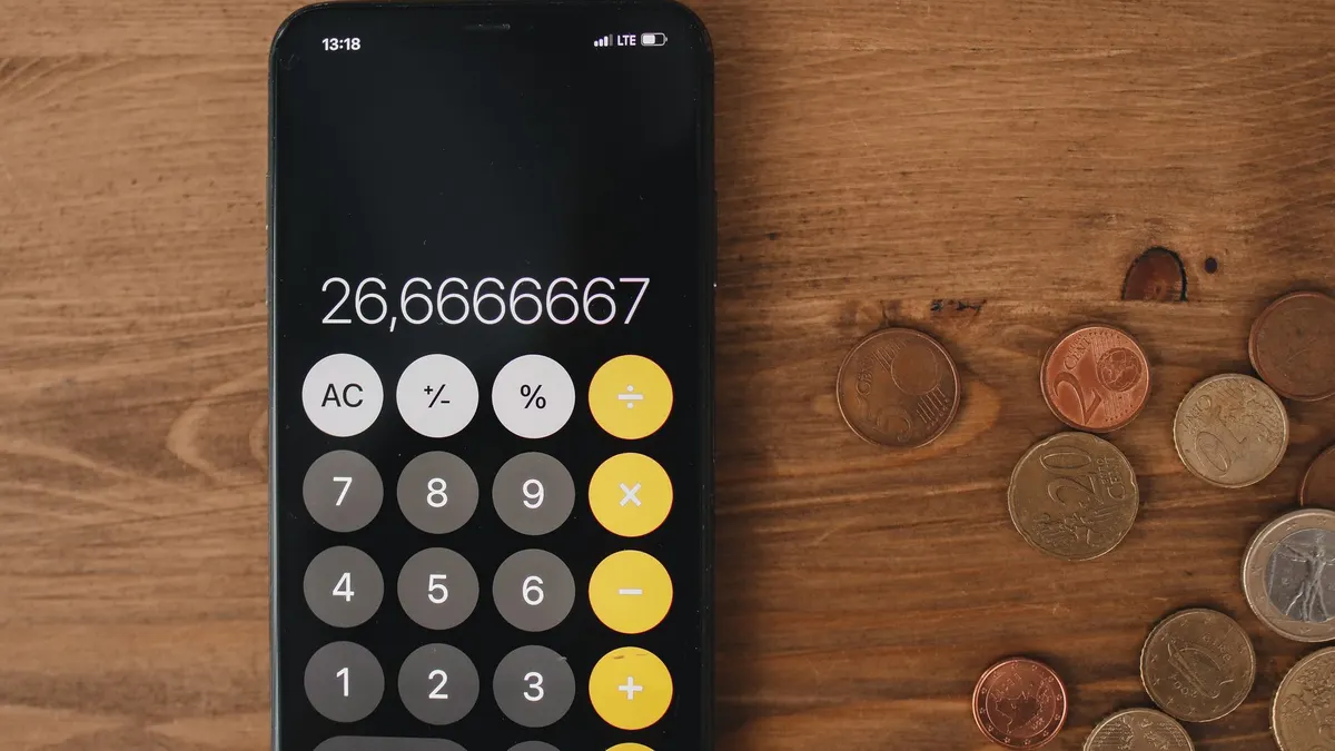 Close-up view of smartphone calculator and coins on wooden surface for financial metaphor.