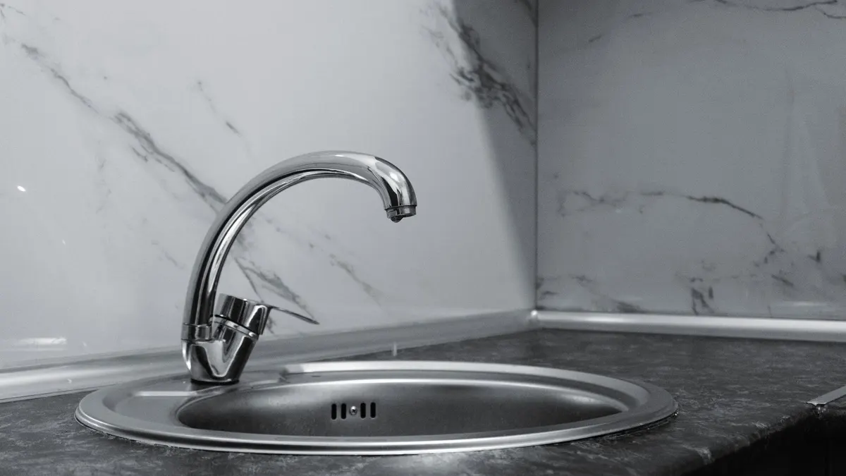 A stylish stainless steel kitchen faucet with a sleek and modern design set against a marble backsplash.