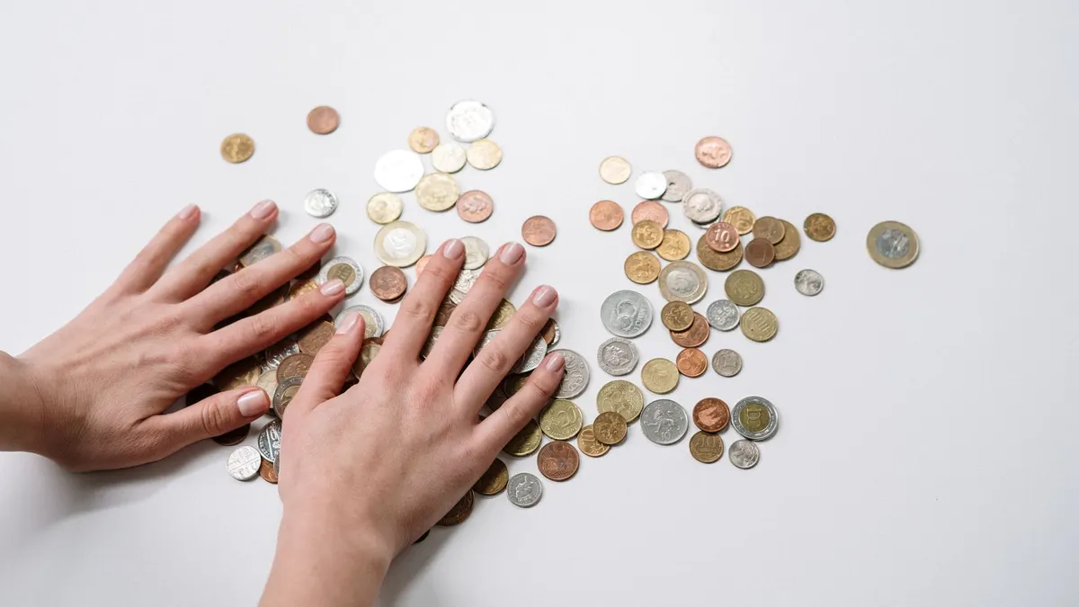 Hands arranging a variety of international coins on a neutral light background.