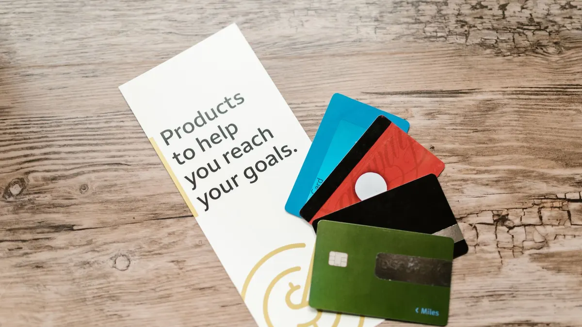 Assorted credit cards on a wooden table next to a leaflet with motivational text about financial goals.