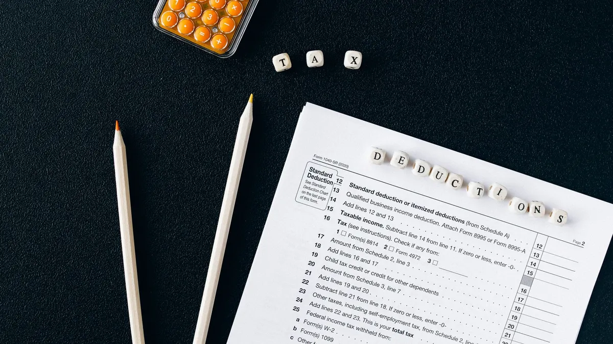 Flat lay of tax form, pencils, and calculator on black background, emphasizing tax deductions.