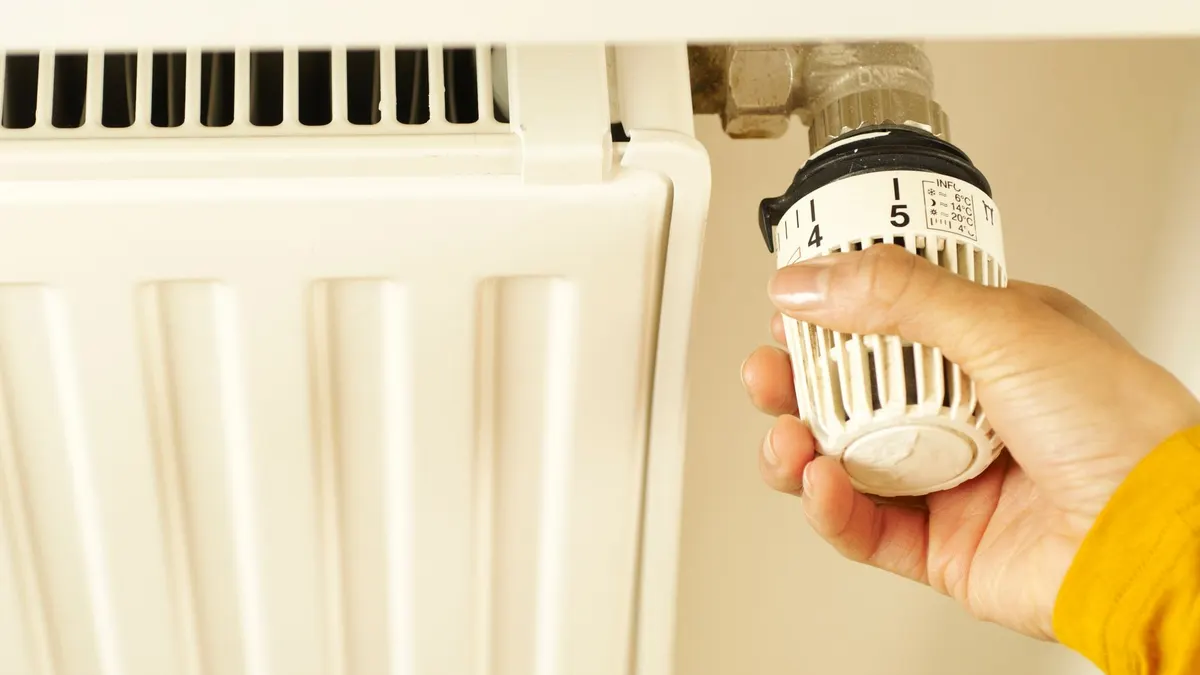Close-up of hand adjusting radiator thermostat to control home heating temperature.