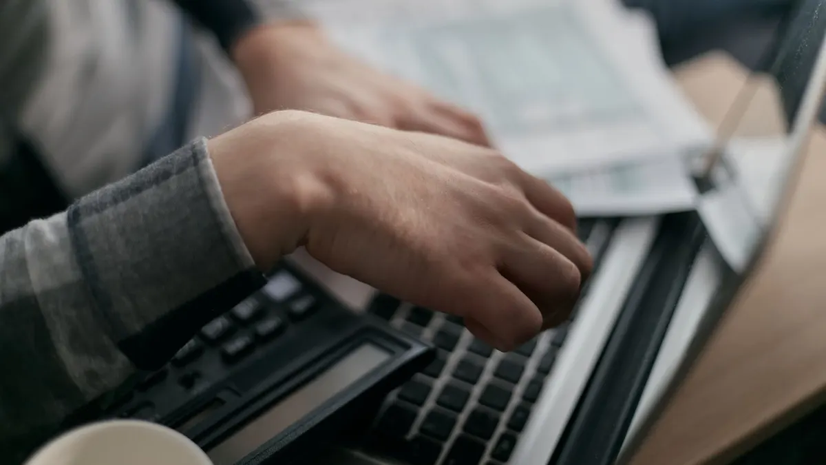 Close-up of hands calculating finances with a laptop and paperwork.