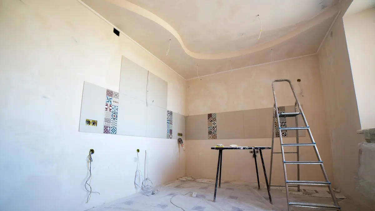 Interior view of a room under renovation with paint, tiles, and tools.