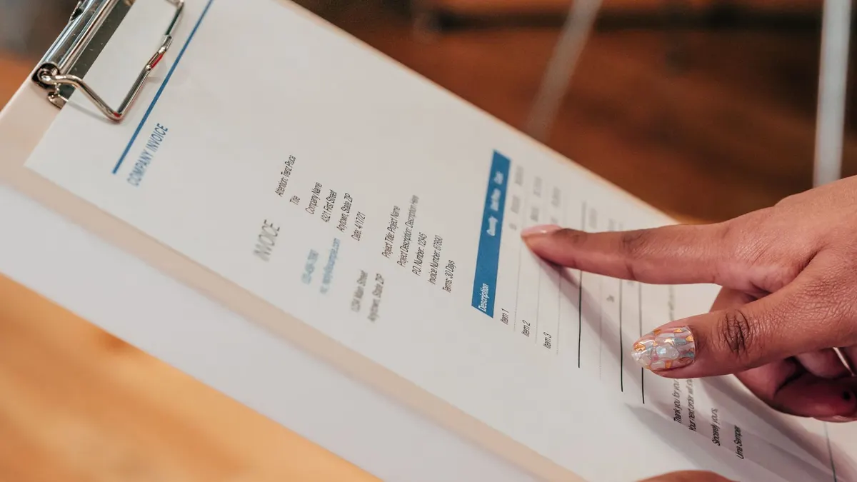 Close-up image of a person pointing to a document on a clipboard, indoors.