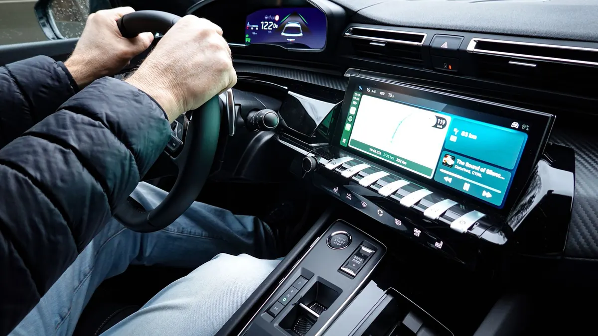 A detailed view of a car's interior with hands on the steering wheel, showcasing modern technology.