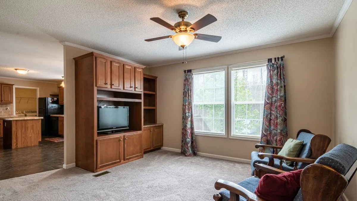 Spacious living room with classic wooden entertainment center and ceiling fan, perfect for a family setting.