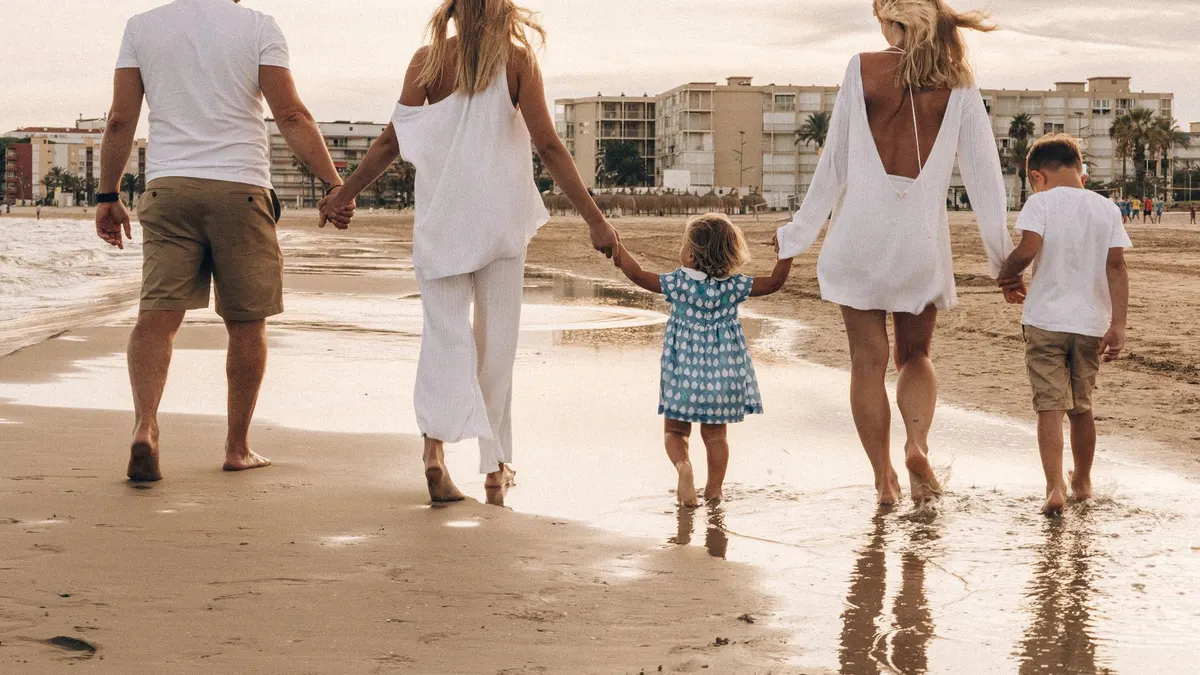 Family walking hand in hand along the beach at sunset, enjoying a warm summer day.