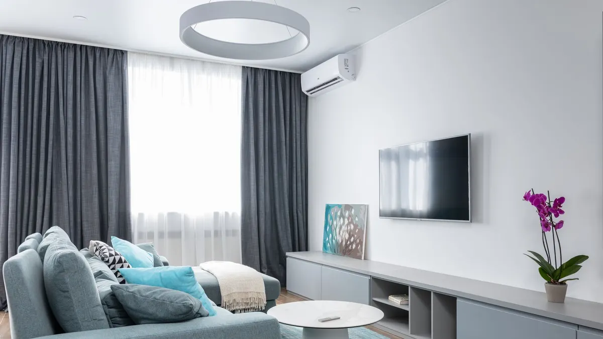 Interior of modern living room with TV on wall and blooming potted flower with picture on shelf