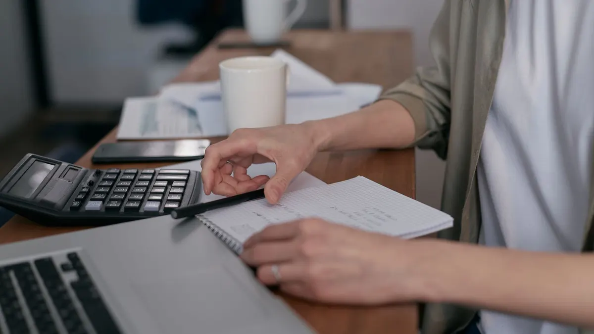 A mid-adult calculating finances with a laptop and notepad, managing budgets at home.