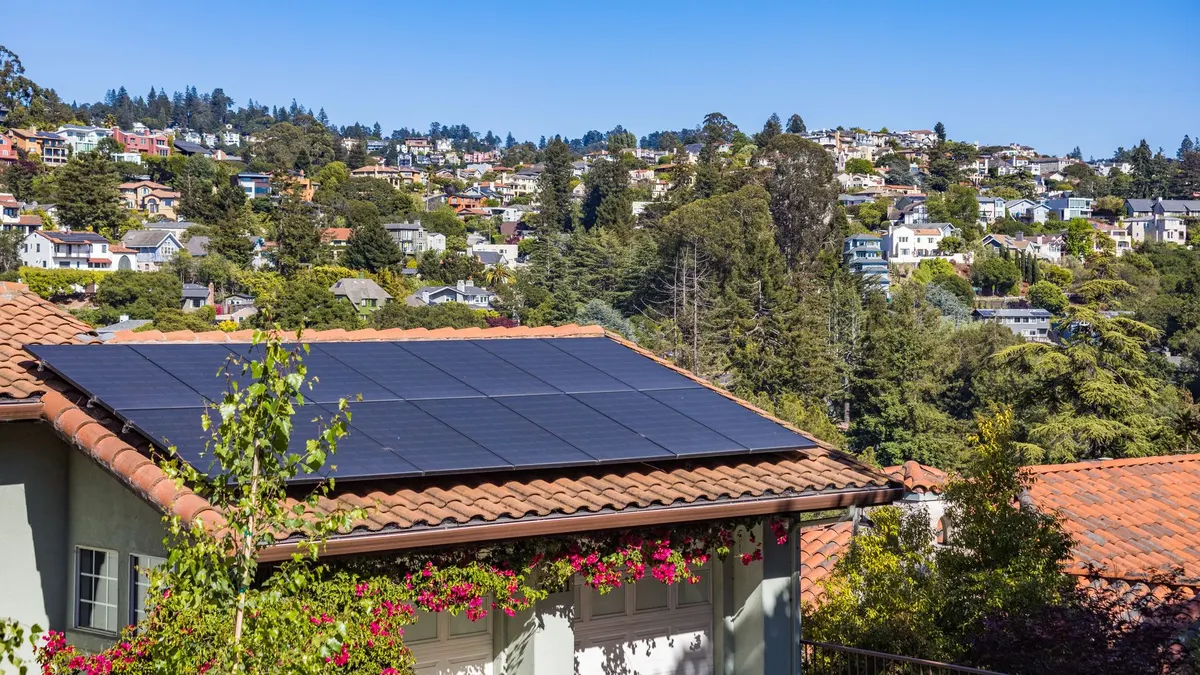 Solar panels on a suburban home, surrounded by lush greenery and a sunny blue sky.
