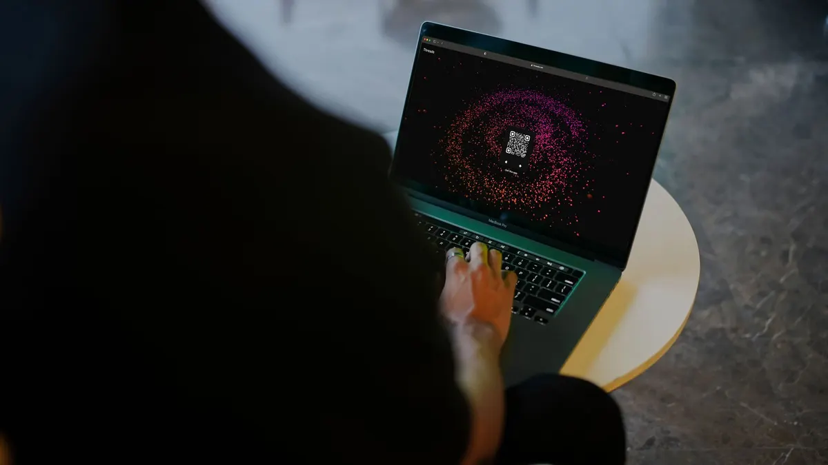 A person interacts with a colorful QR code display on a laptop in a modern indoor setting.