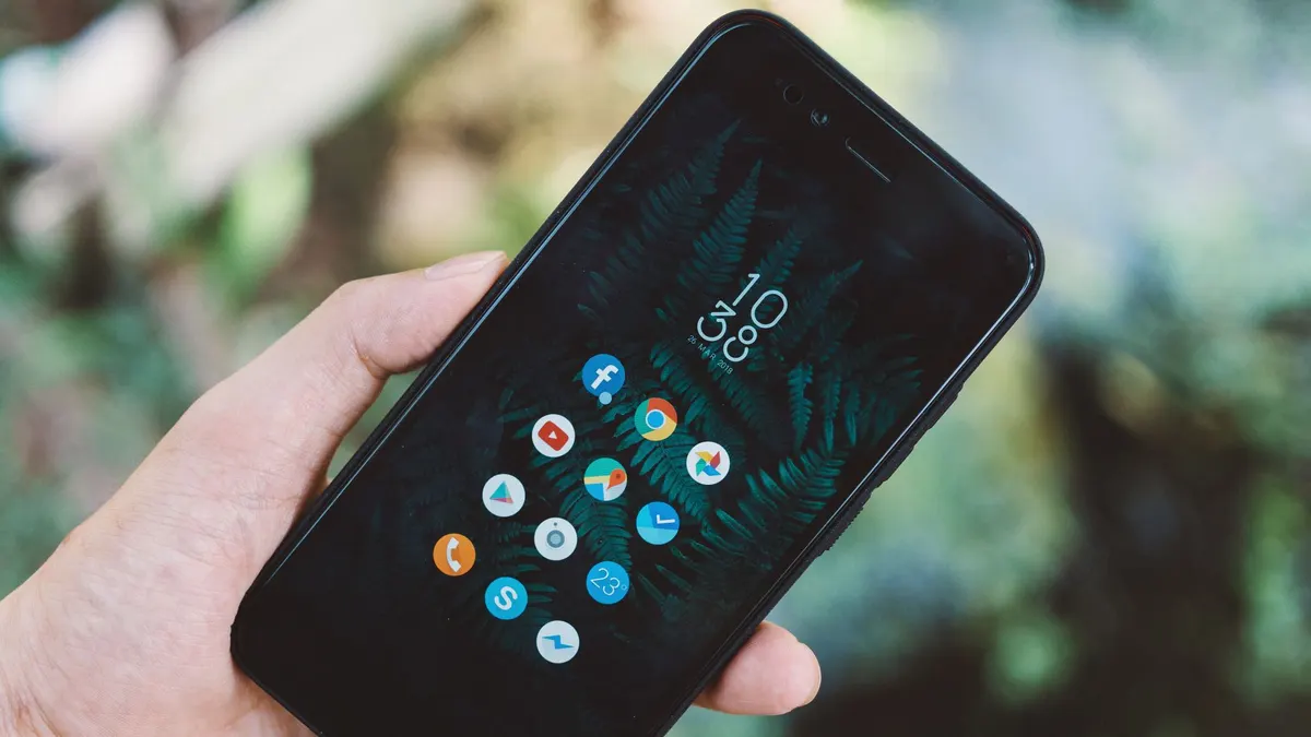 Close-up of a hand holding a smartphone with app icons and a nature wallpaper.