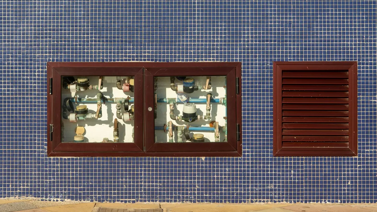 Close-up of a tiled wall with exposed water meters and vent in Arinaga, Spain.