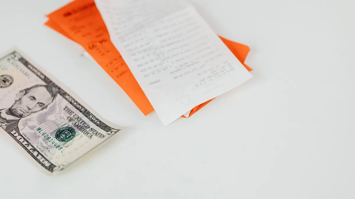 A five dollar bill and receipts on a white surface, emphasizing finance and expenses.