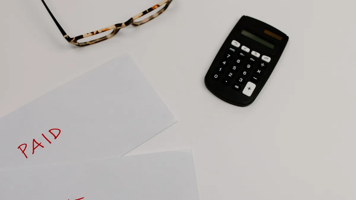 Top view of financial papers labeled 'Paid' and 'Due' beside a calculator and glasses.