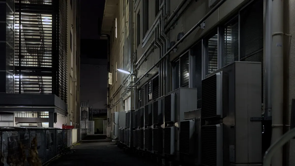 A dimly lit urban alley in Kyoto featuring air conditioning units, captured at night.