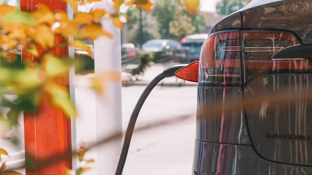 Close-up of an electric car charging at a station with blurred cars in the background.