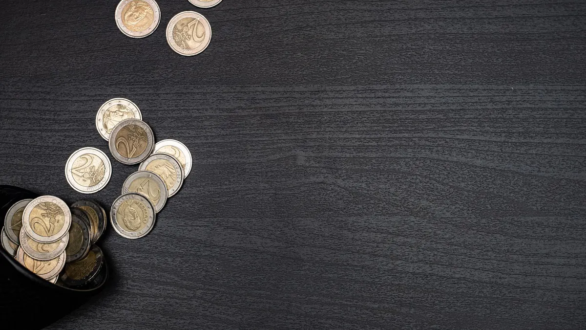 A collection of euro coins scattered on a dark textured surface, with space for text.