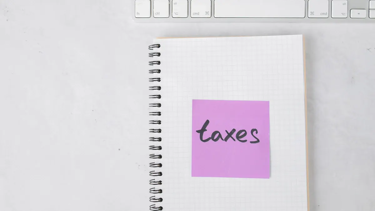 Top view of a notebook with a 'taxes' sticky note beside a keyboard, ideal for finance themes.