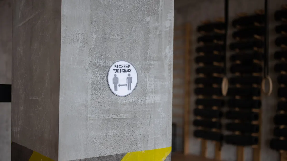 Round sign with Please Keep Your Distance title and arrow between figures on post during coronavirus pandemic in gymnasium