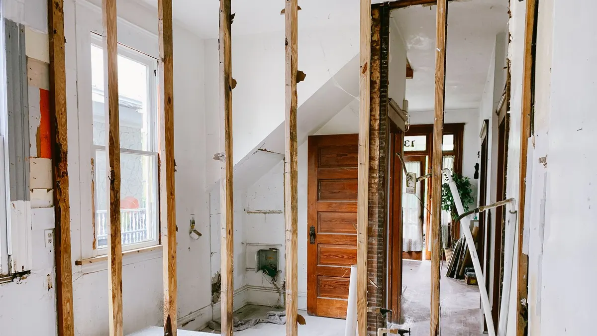 Interior view of a home under renovation with exposed wooden beams and door.