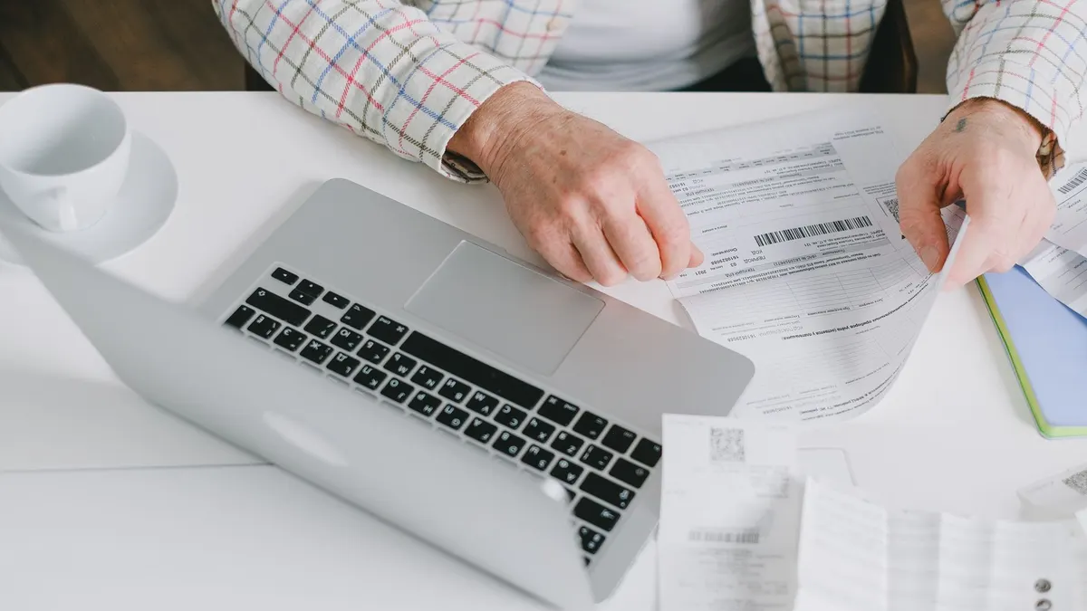 Close-up of hands organizing documents on a desk with a laptop.