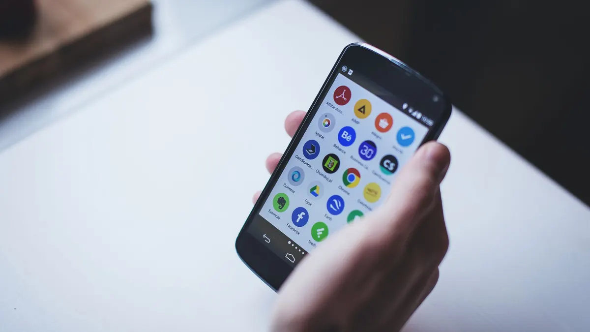 Close-up of a person holding a smartphone with various app icons visible on the screen.