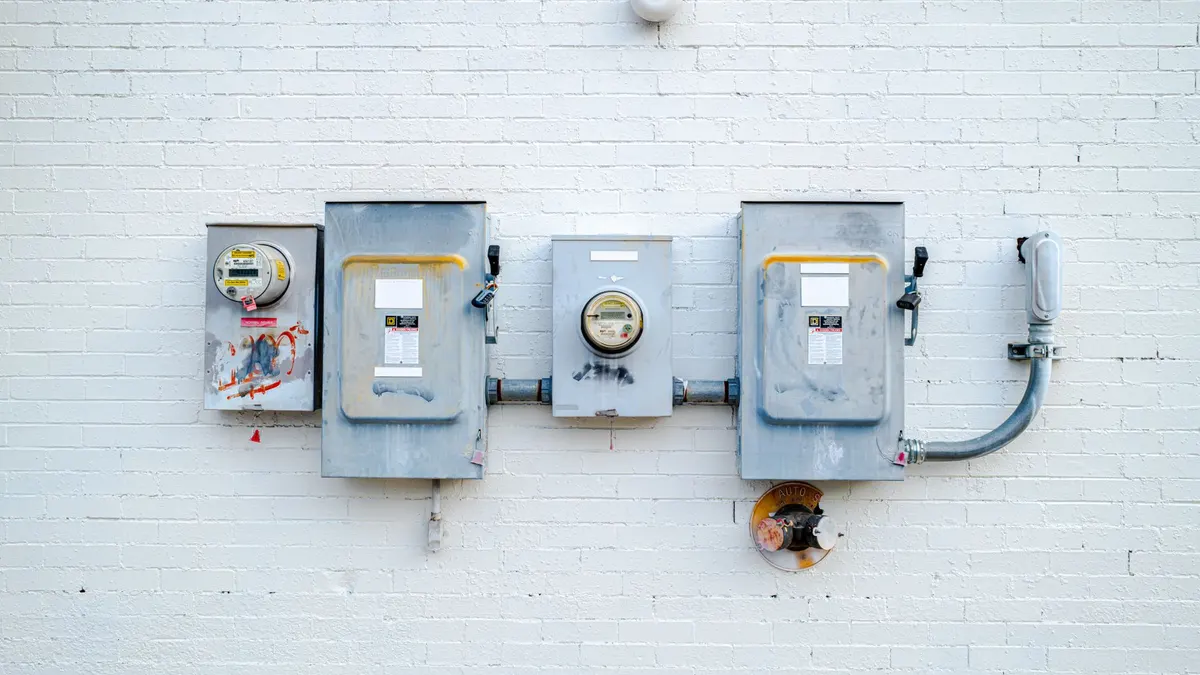 Electrical boxes and power meters mounted on a white brick wall.