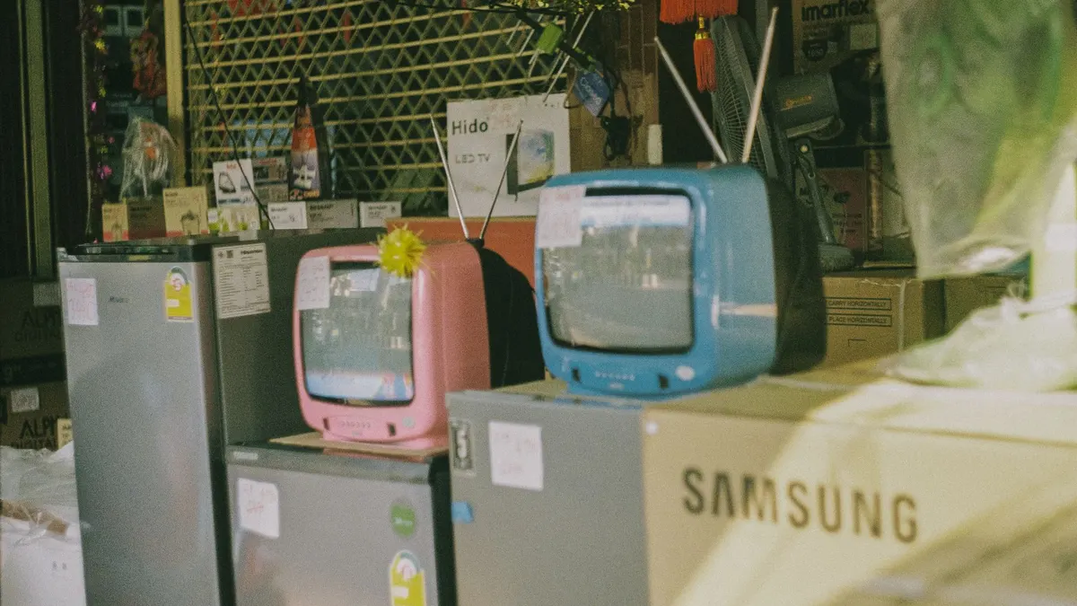 A storefront display featuring vintage televisions and home appliances on a sunny day in Bangkok.