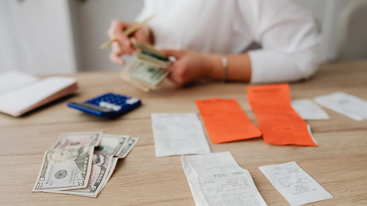 A person using a calculator and cash to plan a household budget.