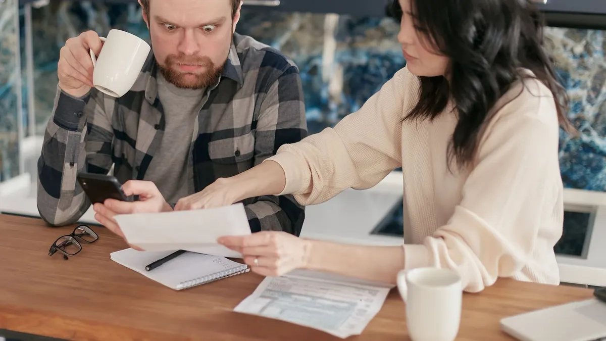 A couple reviews household bills in a kitchen, appearing concerned and focused.