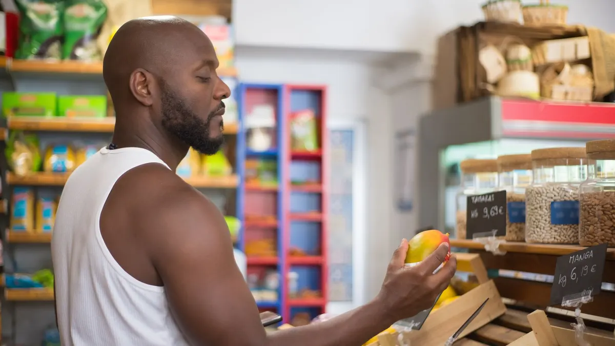 Adult man shopping for mangoes in a Portuguese supermarket, examining fruit quality.
